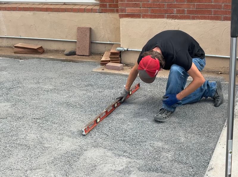 Checking a compacted gravel base with a level before hardscape installation in Albuquerque